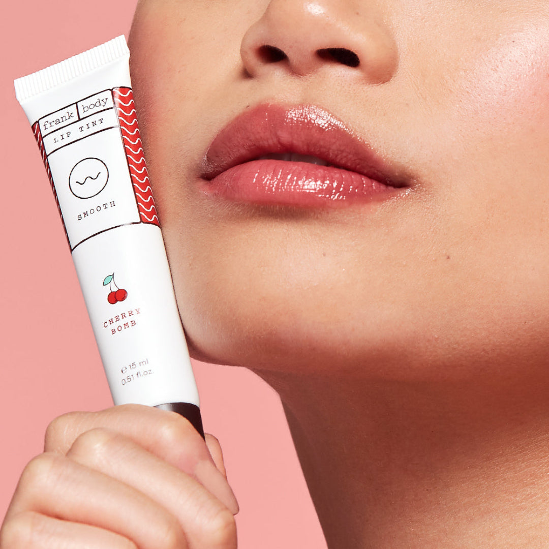Lip balm with cherry design held by a hand, against a pink background