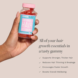 A hand holding a bottle of Hair Burst Chewable Hair Vitamins gummies against a solid beige background, with promotional text detailing hair growth benefits.