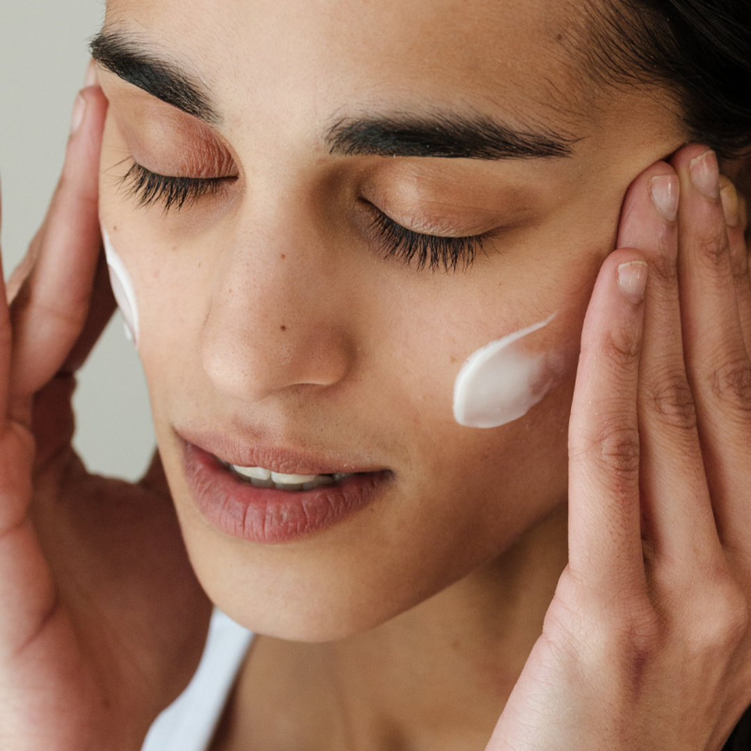 Woman applying cream to her face with a neutral background