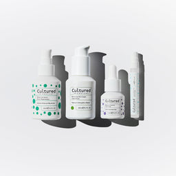 Four white pump bottles from the brand Cultured, arranged vertically in a staggered pattern with dark gray drop shadows on a light gray background.