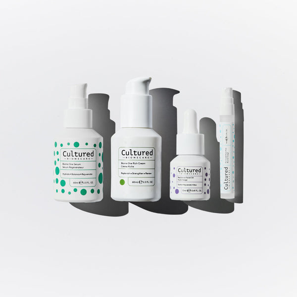 Four white pump bottles from the brand Cultured, arranged vertically in a staggered pattern with dark gray drop shadows on a light gray background.