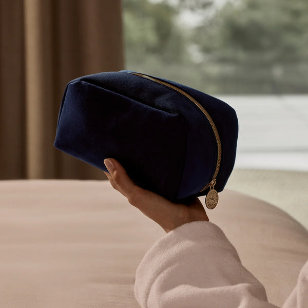 Navy blue pouch with gold zipper held by a person in a soft-focus indoor setting