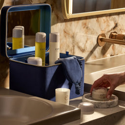 Bathroom scene with a blue toiletry bag, ESPA products, and a hand holding a jar.