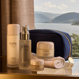 ESPA skincare products with a blue pouch and towel on a reflective surface with a scenic background.