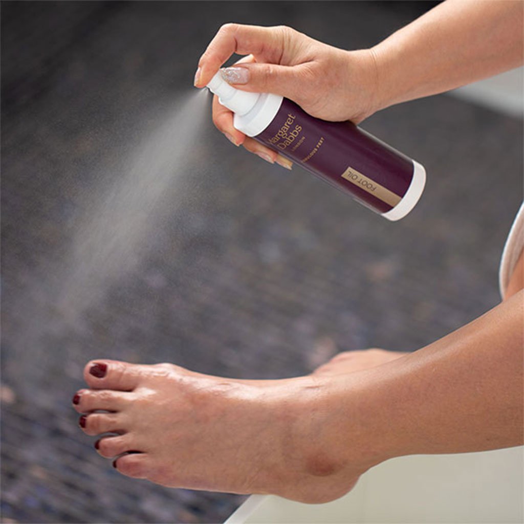 Person applying a spray product to their foot with a blurred background