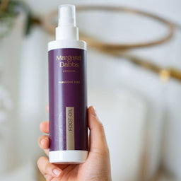 Hand holding a bottle of Margaret Dabbs London foot oil with a blurred background