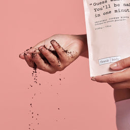 a hand holding the coffee scrub while grains fall through their finger tips