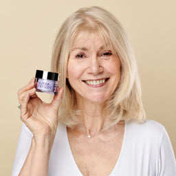 Model holding the retinol day cream jar next to her face while smiling