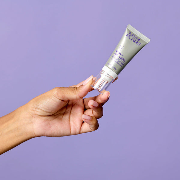 Model holding retinol eye cream upwards diagonally against purple background